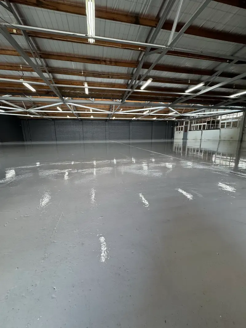 Completed grey commercial-grade epoxy floor running the length of the Oakleigh warehouse, reflecting the overhead lighting