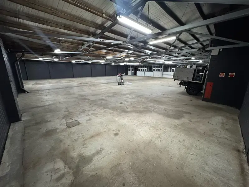 Bare concrete floor of the Oakleigh warehouse before epoxy coating, with preparation equipment and a ute on site.